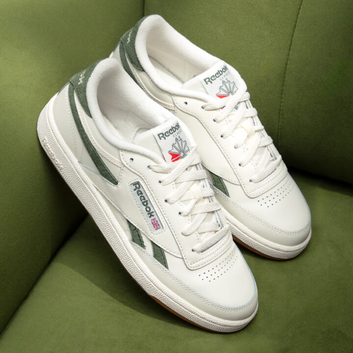 White Reebok Classic trainers with green stripes over a green background