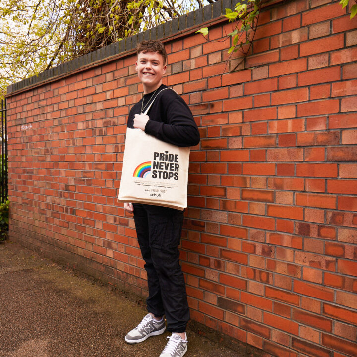 Person standing in front of red brick wall carrying pride tote bag