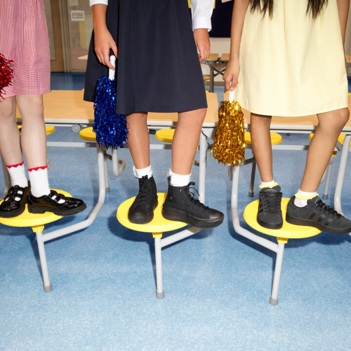 Three kids standing on top of chairs in black shoes