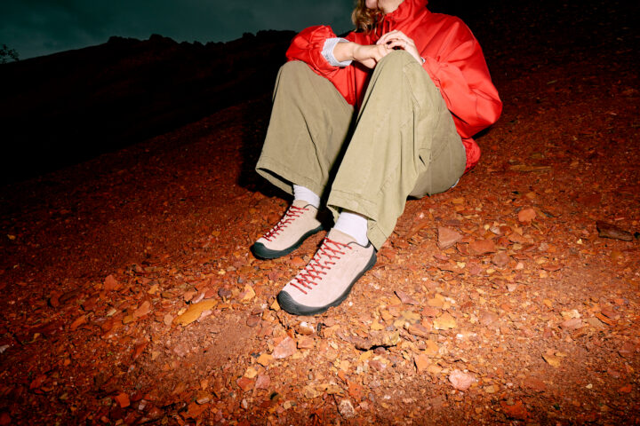 Person wearing beige KEEN Jaspers with beige trousers and a orange jacket, sitting outside.
