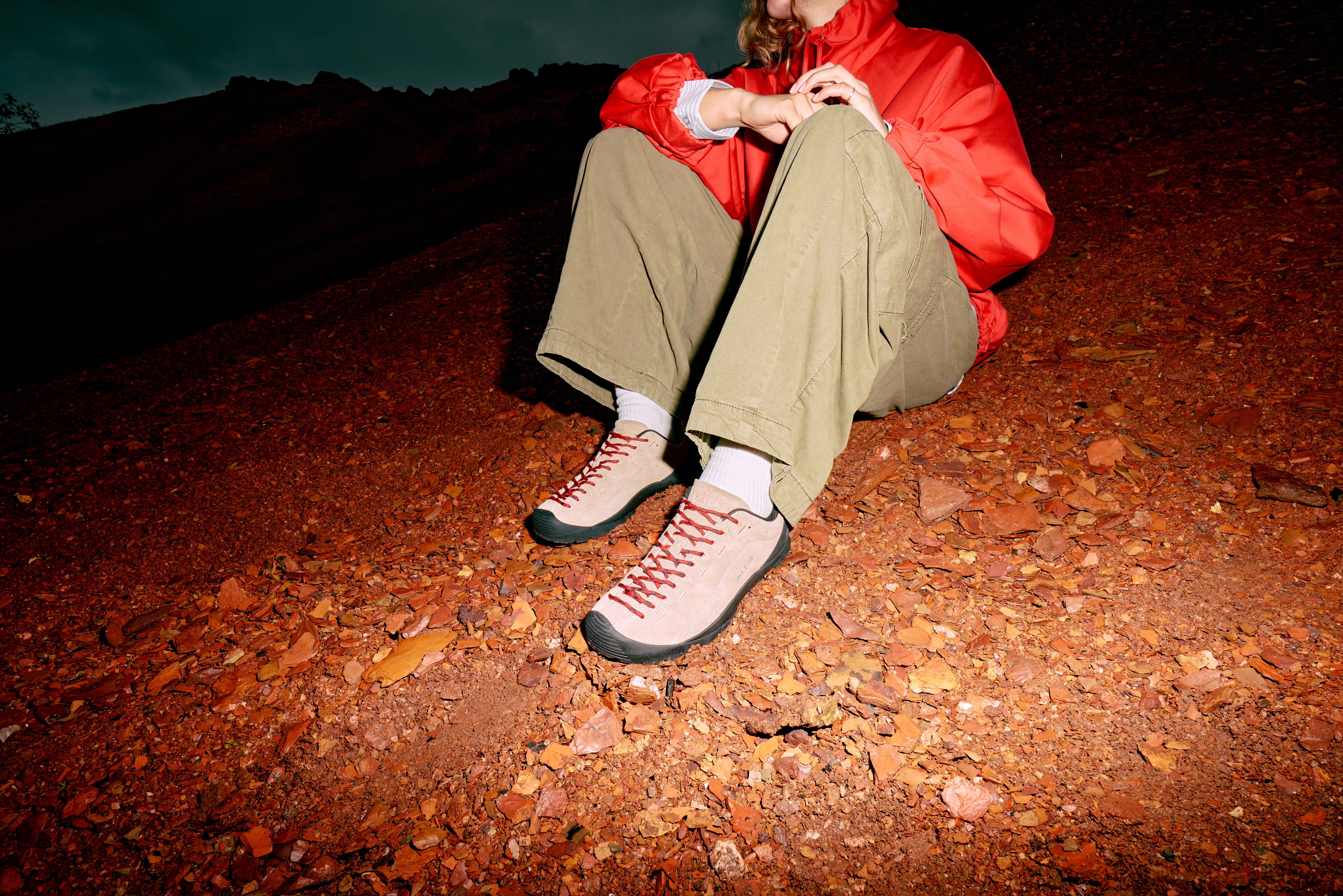 Person wearing beige KEEN Jaspers with beige trousers and a orange jacket, sitting outside.