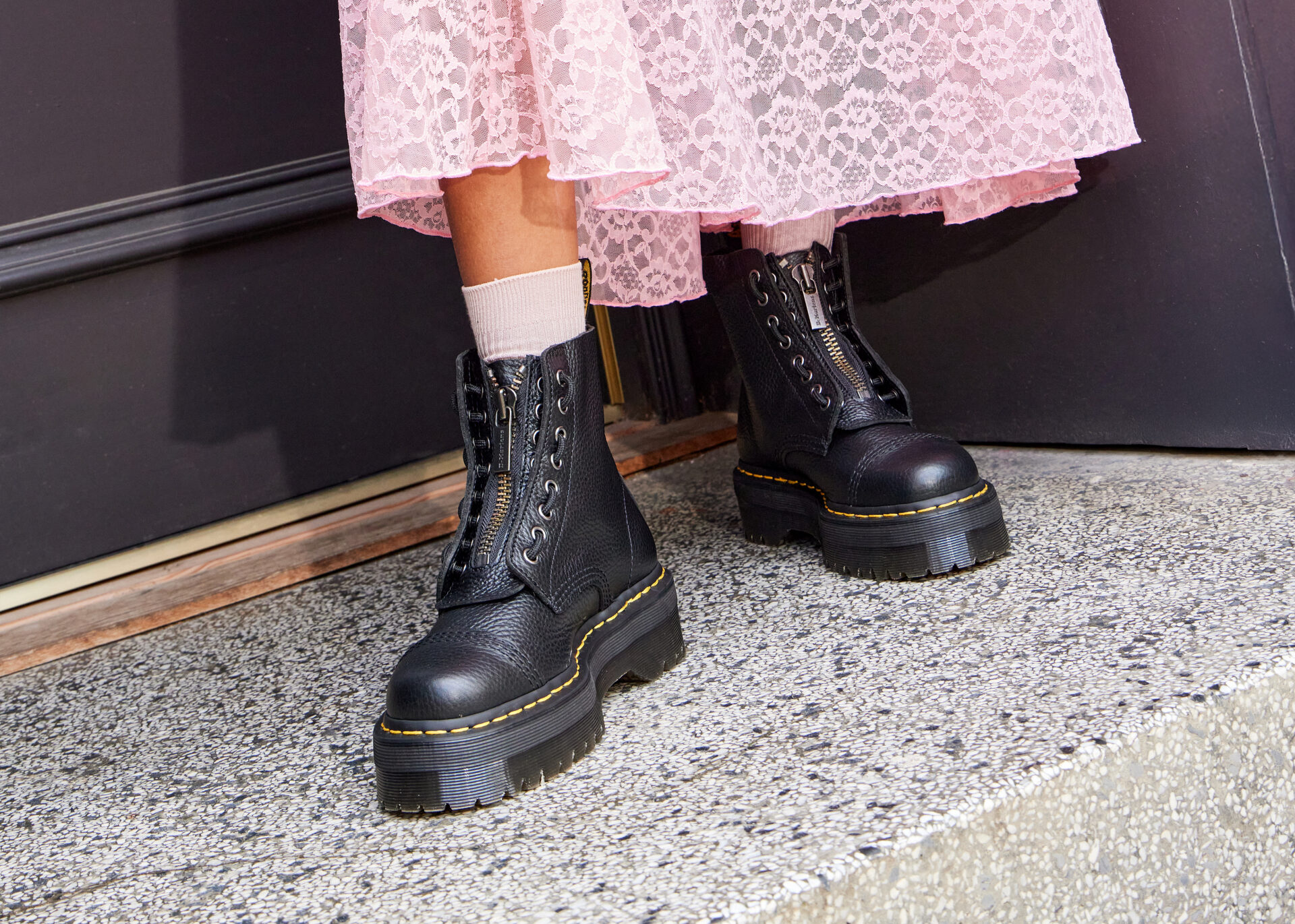 Person wearing platform Dr. Martens boots in black with white socks and a long pink lace skirt.