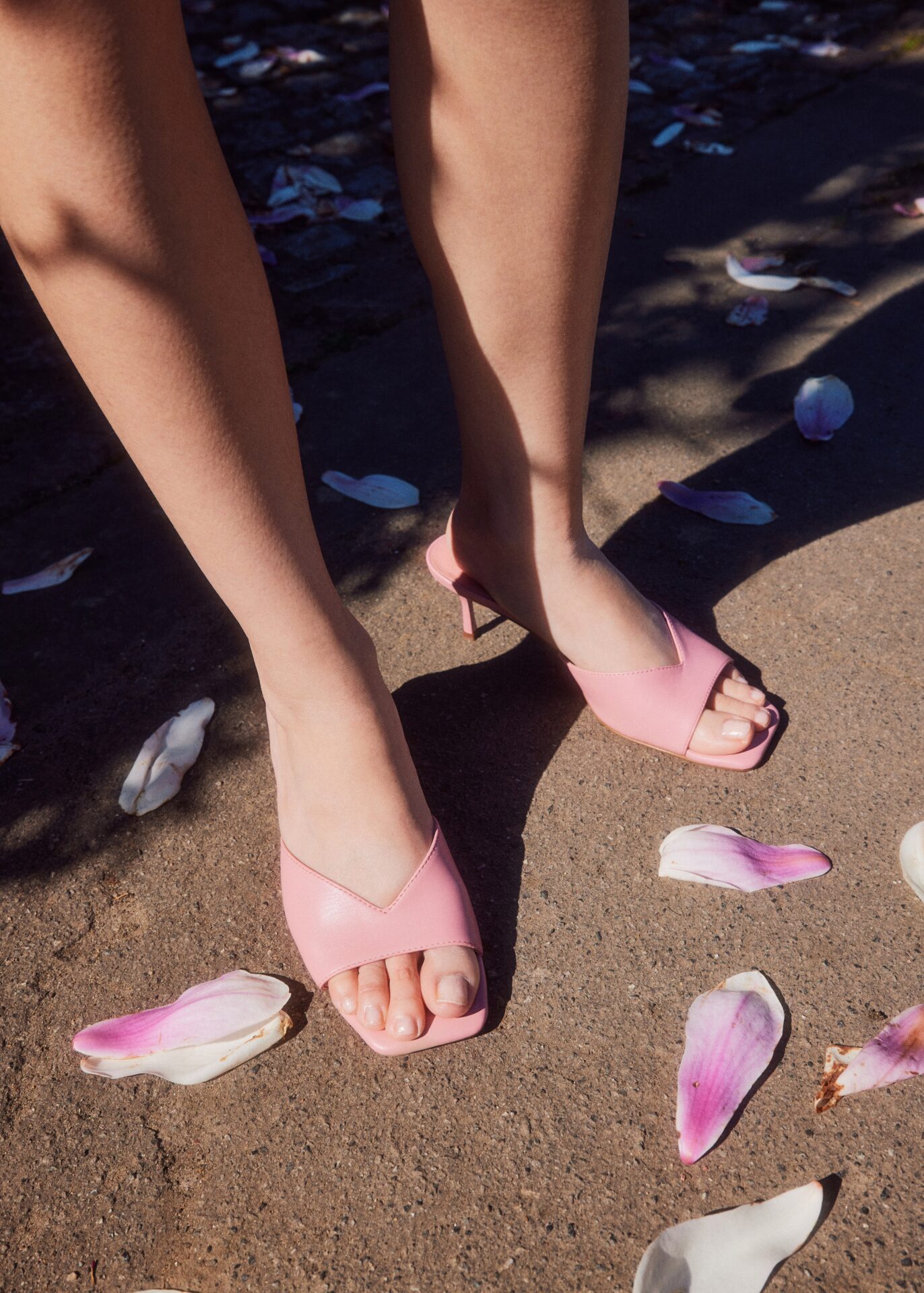 Person wearing light pink heels, standing outside with flower petals around.