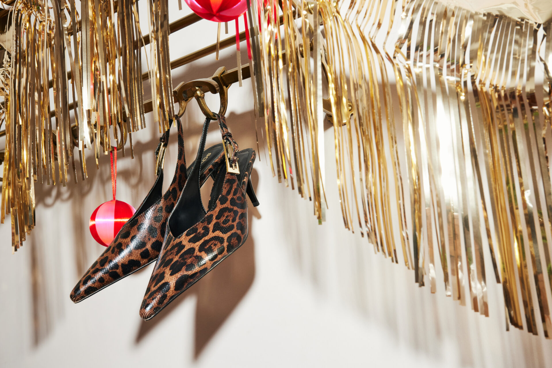 The schuh Sage Buckle Slingback Court in leopard print hanging next to Christmas decorations.