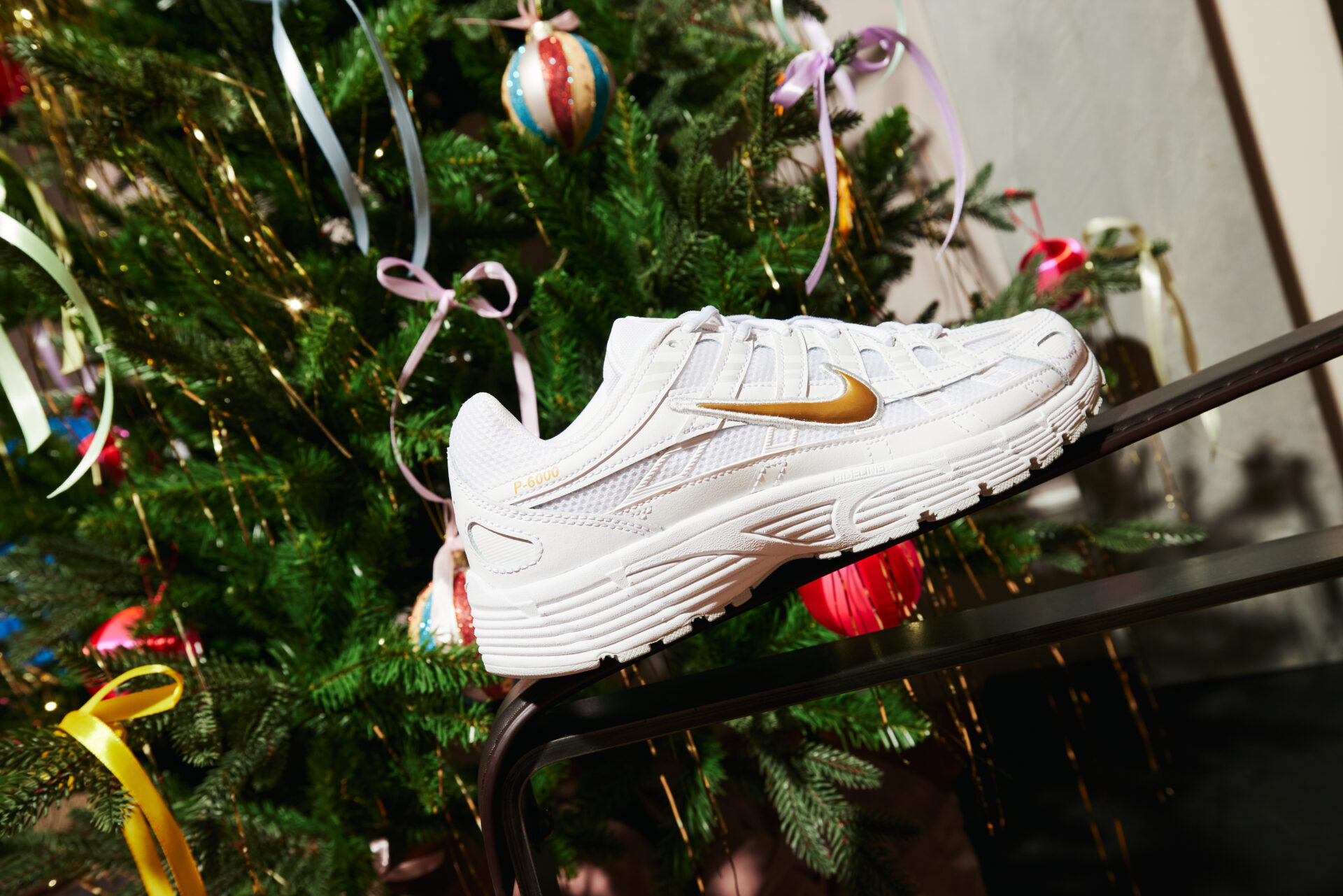 A white and gold Nike P-6000 sitting near a Christmas tree.
