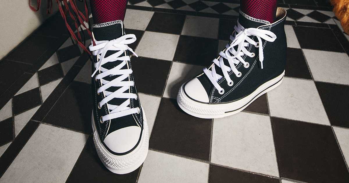 Person wearing black Converse All Star Hi trainers with red fishnet socks.