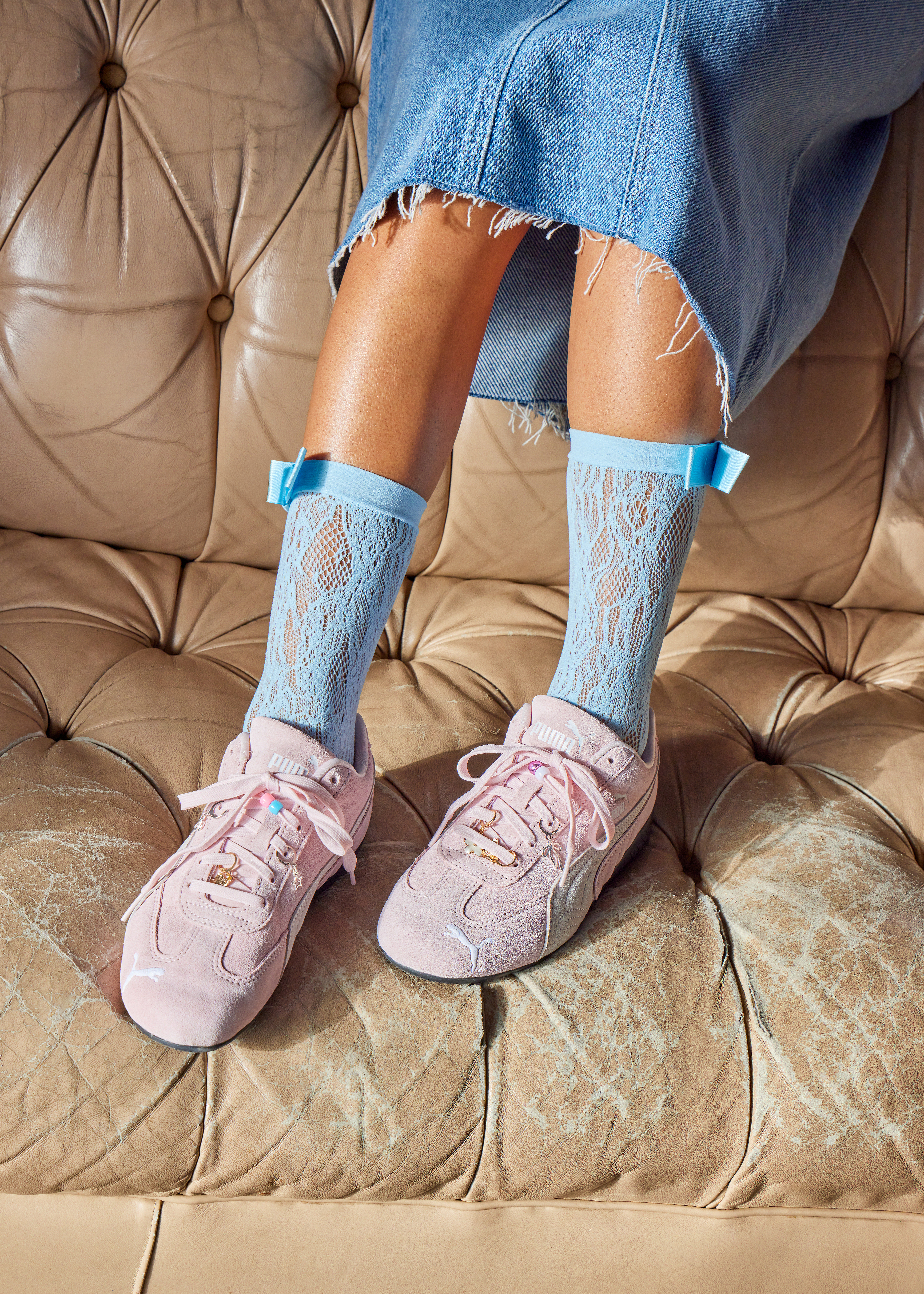 Person wearing a pink PUMA Speedcat with charm details with lace blue socks and a long denim skirt.