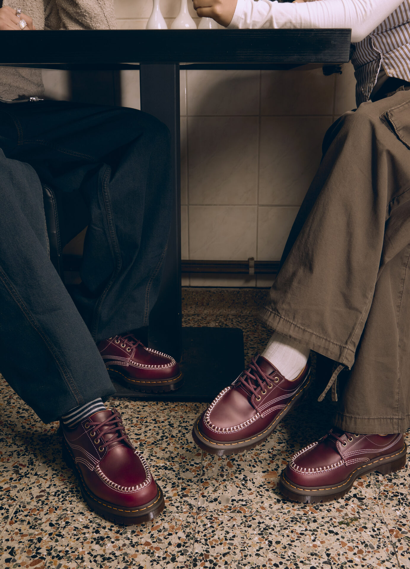 Two people wearing the Dr. Martens Lowell in cherry red, one with blue jeans and one with khaki cargo trousers.
