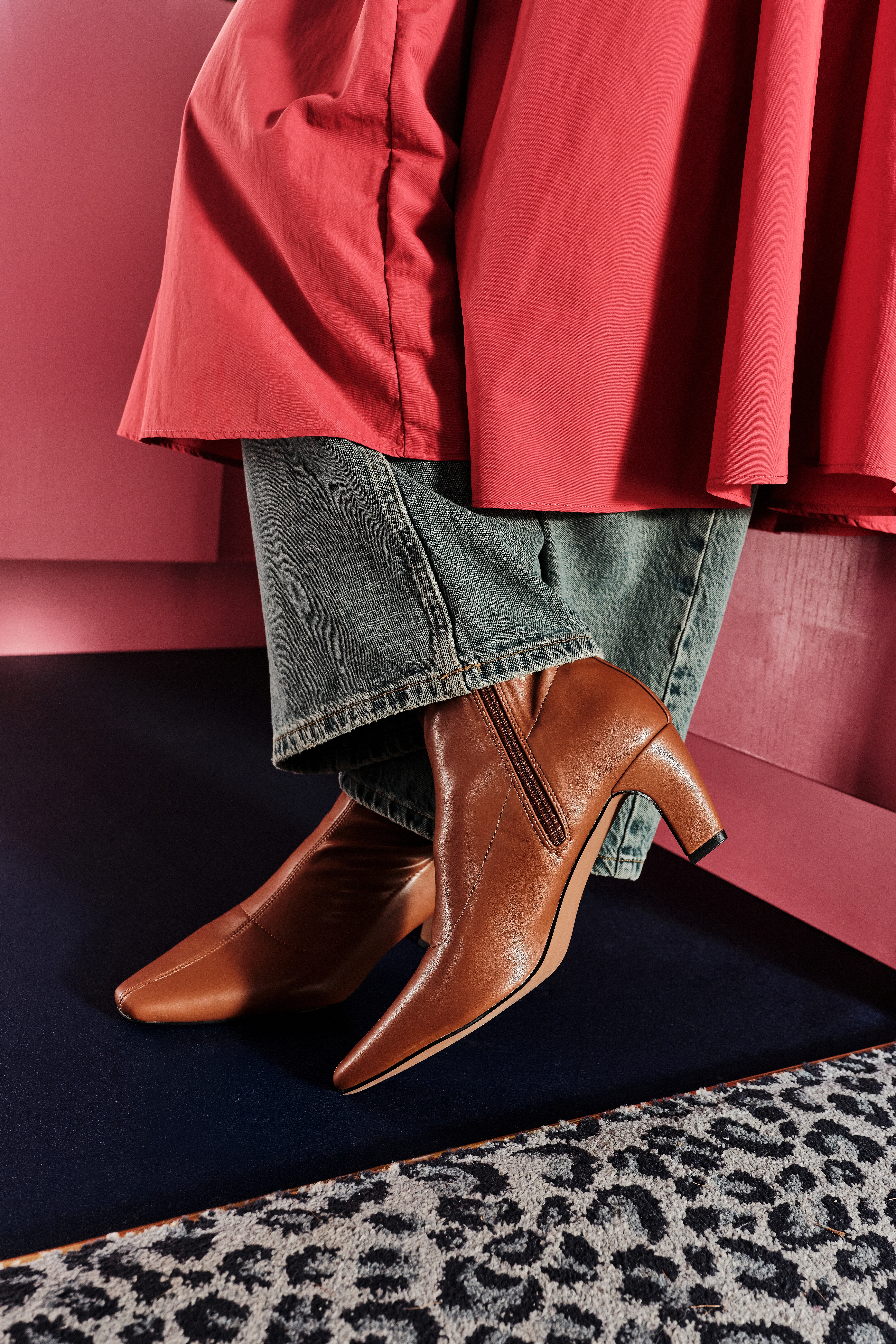 Person wearing a heeled brown boot with wide leg jeans and a long red skirt.