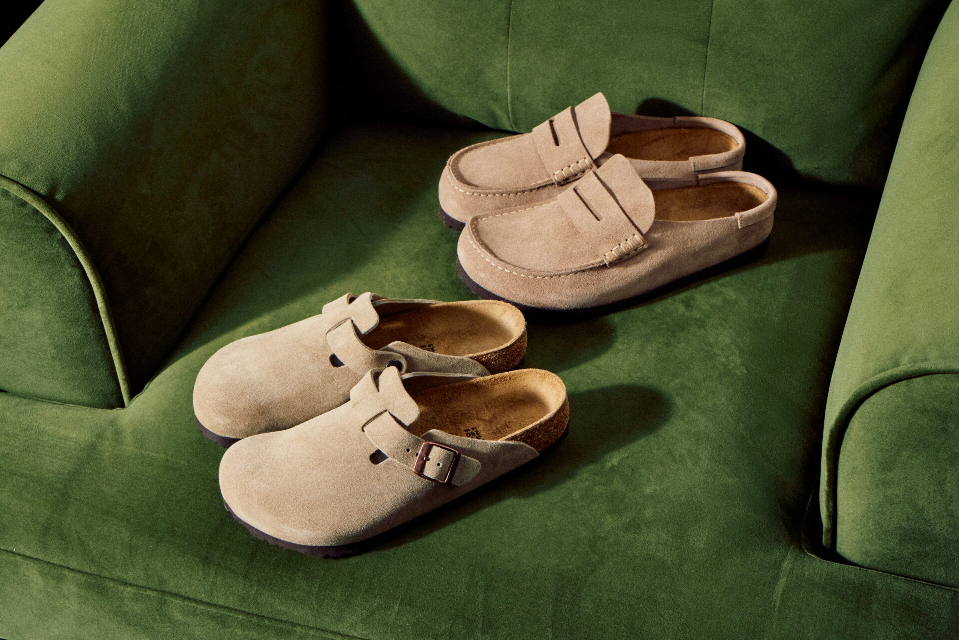 A pair of BIRKENSTOCK Boston and Naples in taupe, sitting on a dark green chair.