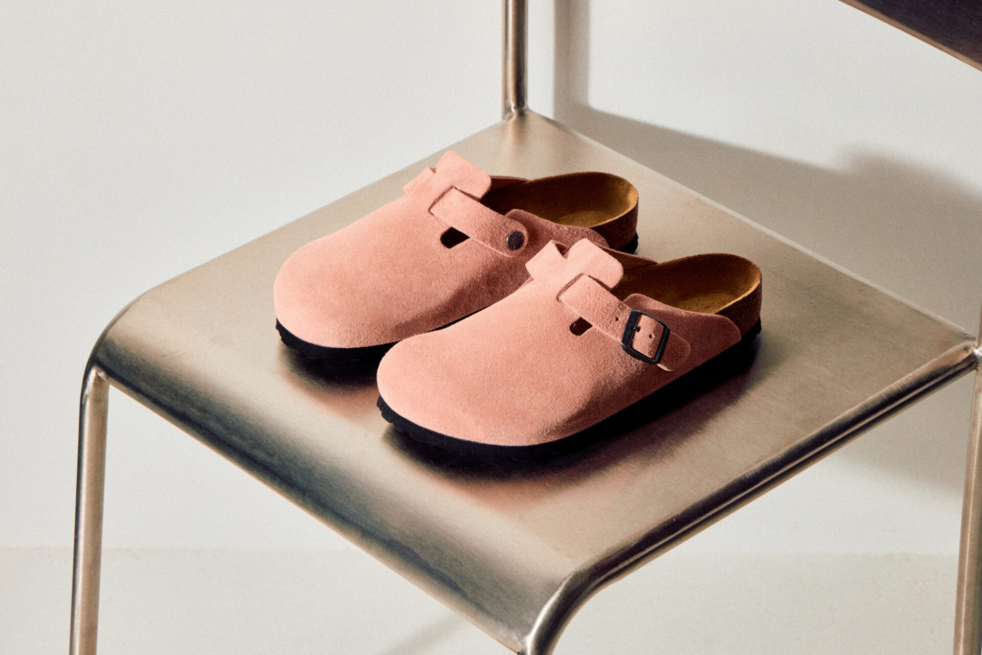 A pair of BIRKENSTOCK Boston in pink sitting on a metal chair.