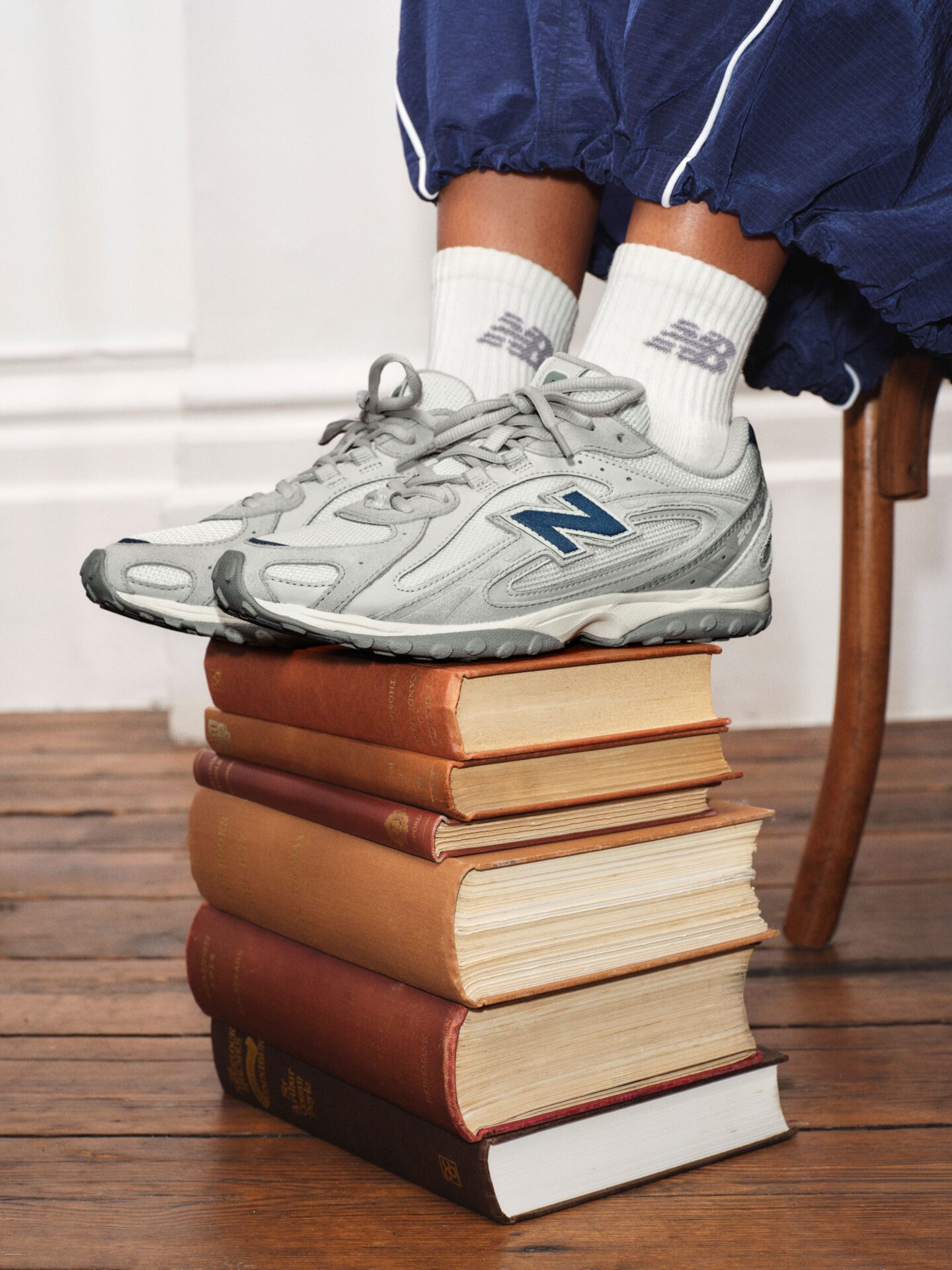 The New Balance 204L in grey and blue worn with white NB socks and navy track pants, sat on top of a stack of books.
