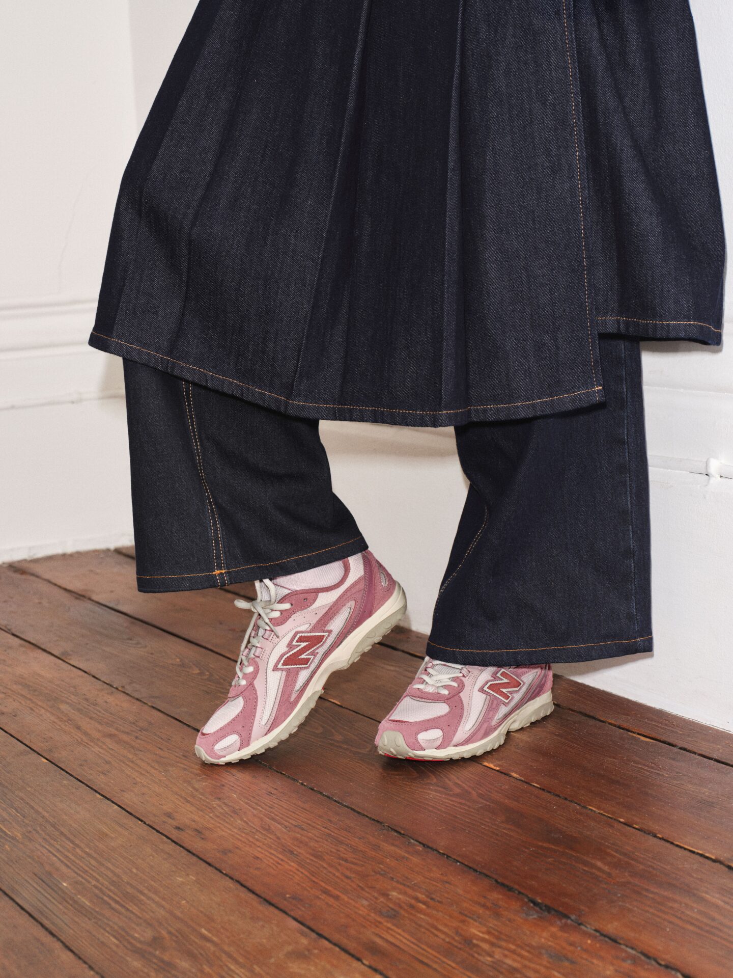 A person wearing the New Balance 204L in pink with dark blue jeans and a matching long denim skirt.