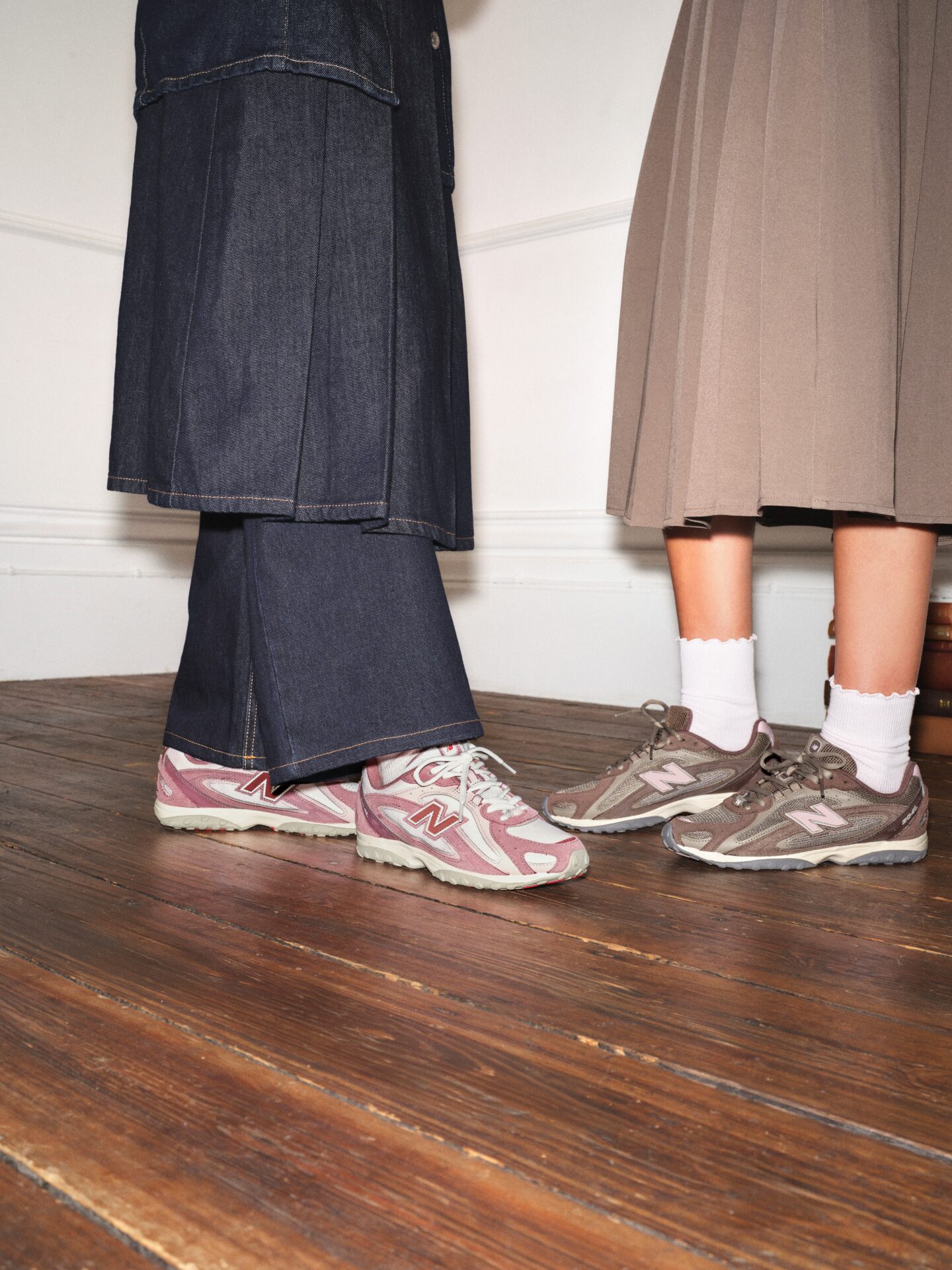 A person wearing the New Balance 204L in pink with dark blue jeans and a matching long denim skirt, next to a person wearing the New Balance 204L in brown with a brown midi skirt and white socks.