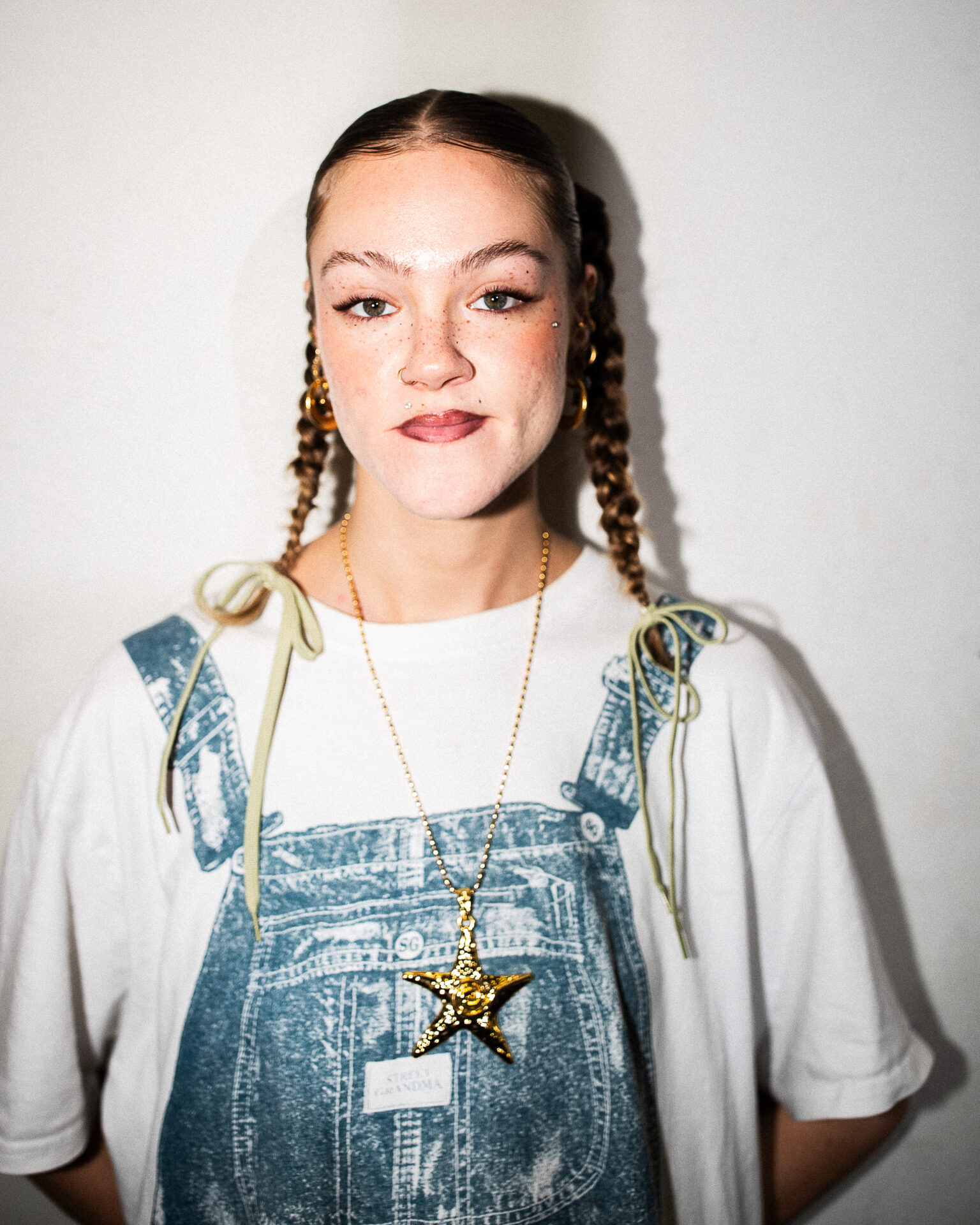 Lili wearing a white and blue printed t-shirt, green hair bows, and gold jewelry. 