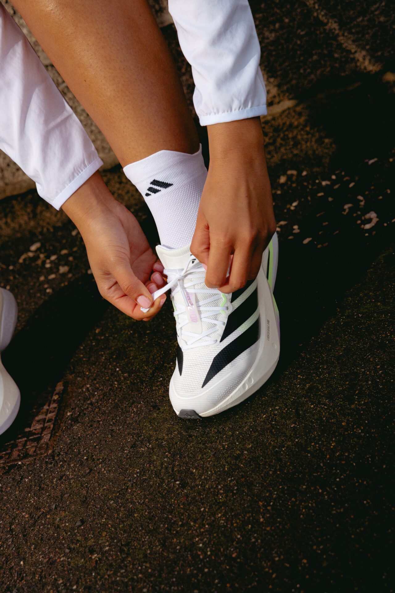 Person lacing up a pair of white and black adidas Adizero trainers.