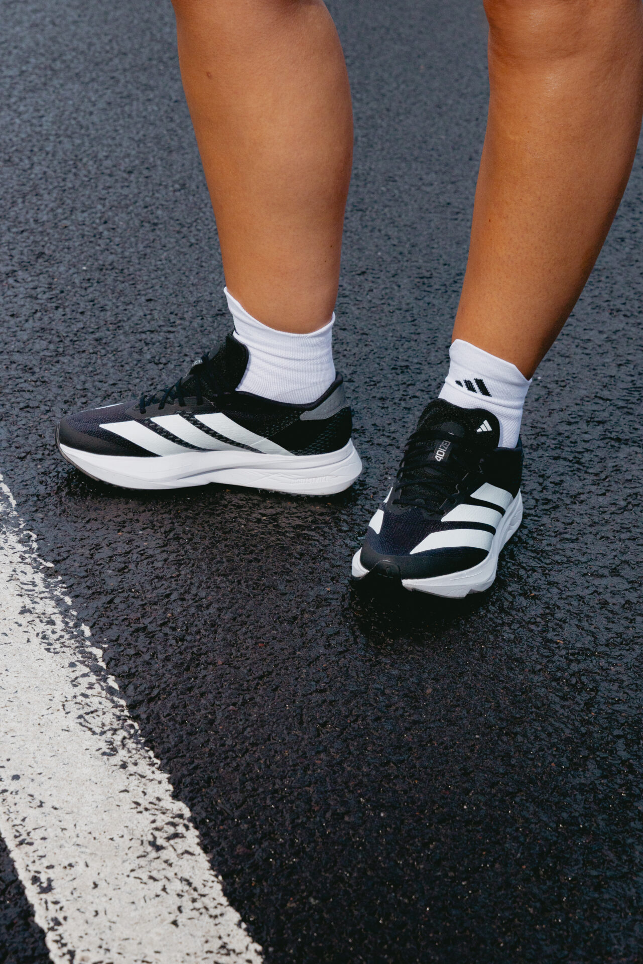 Person standing outside wearing black adidas running trainers paired with white adidas socks.