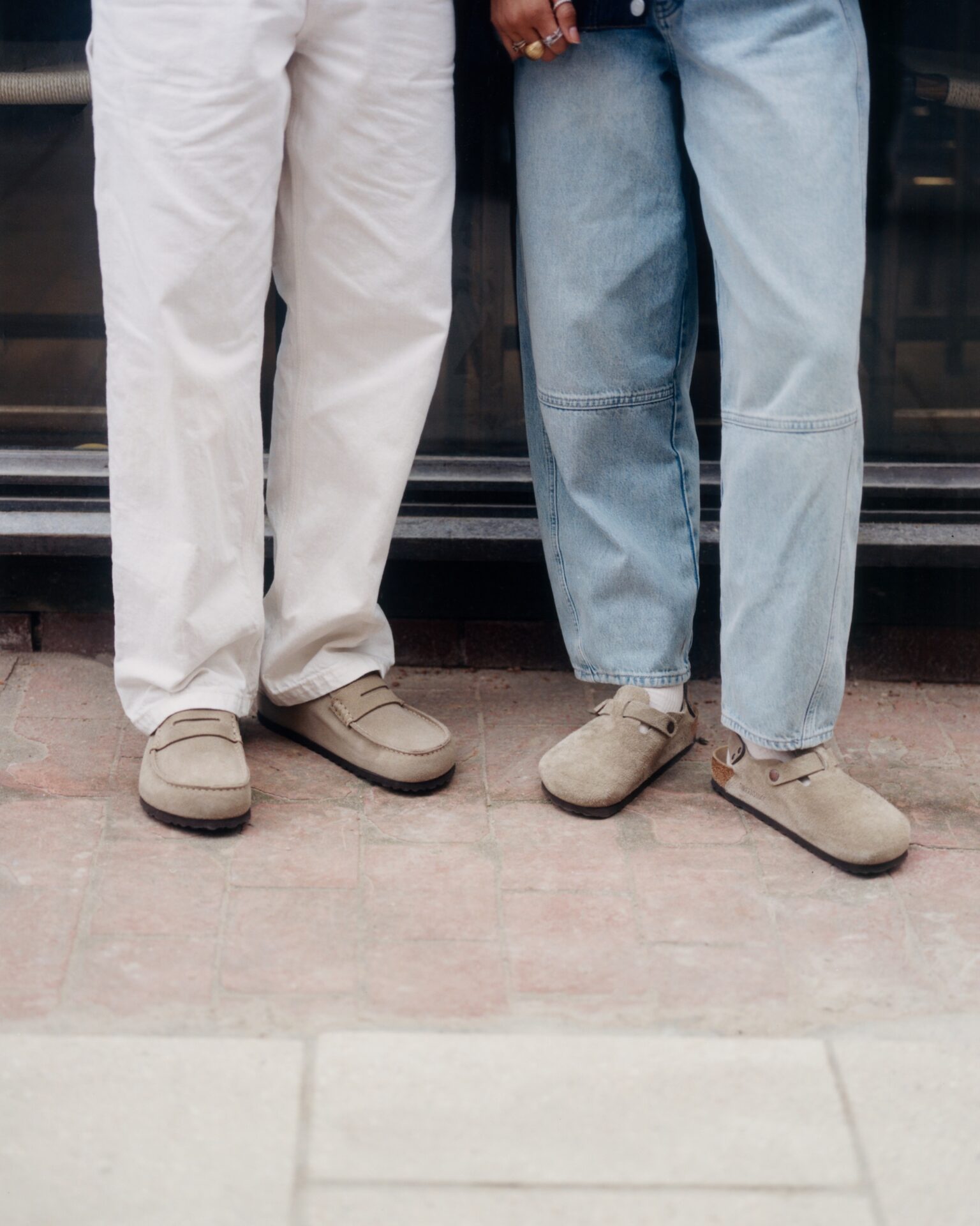 One person wearing BIRKENSTOCK Naples in beige with white trousers, standing next to someone wearing BIRKENSTOCK Boston in beige with light blue jeans and white socks.