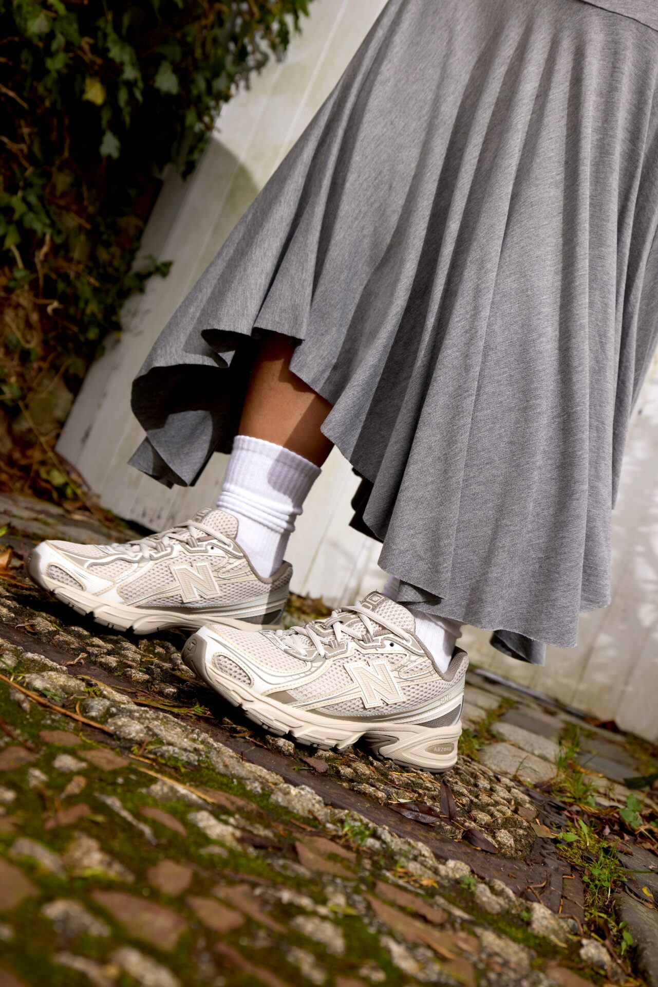 Person standing outside wearing beige New Balance 740 trainers with a long grey skirt.