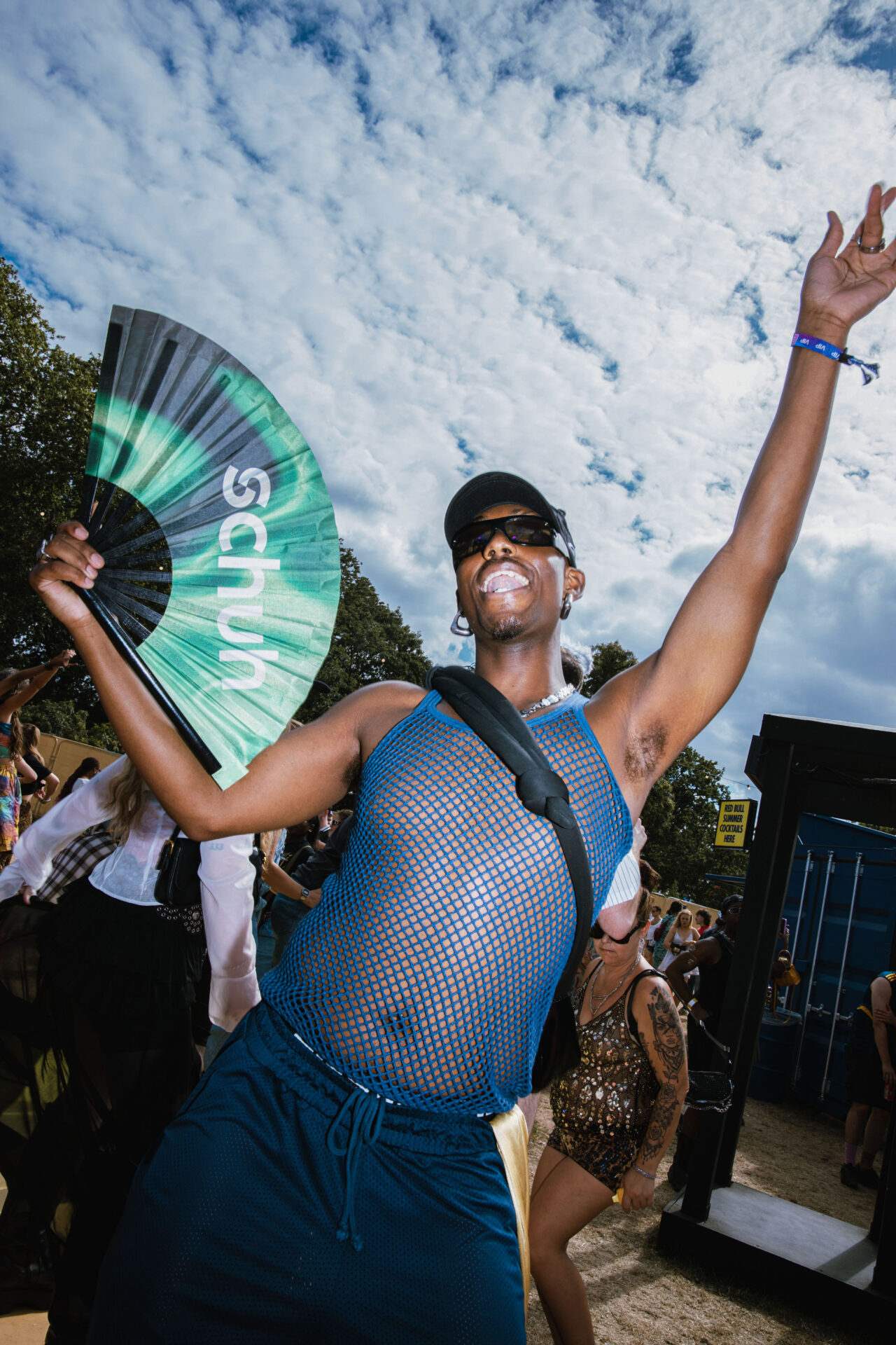 A person standing and holding a green schuh paper fan while wearing a summery outfit at Mighty Hoopla festival.