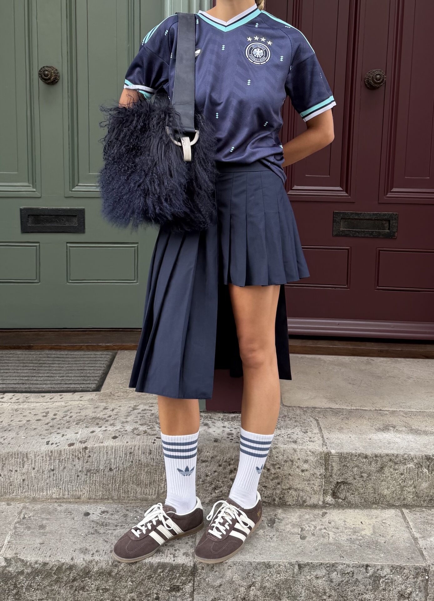@torivanbreugel wearing the brown adidas Gazelle Lo Pro with white adidas socks, an asymmetric pleated navy blue skirt, and a navy Germany football top.