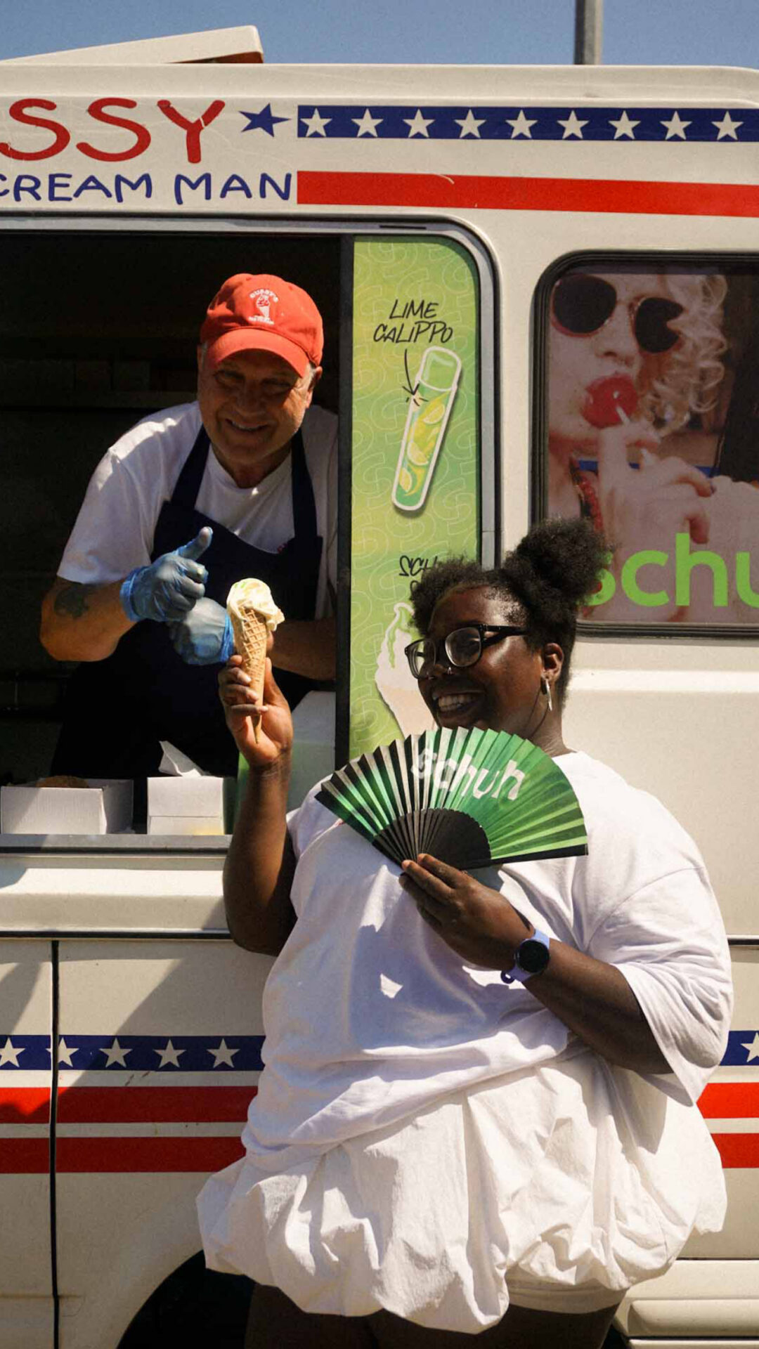 A member of the SheCanServe community holding a schuh branded fan, standing with Gussy in his ice cream van.