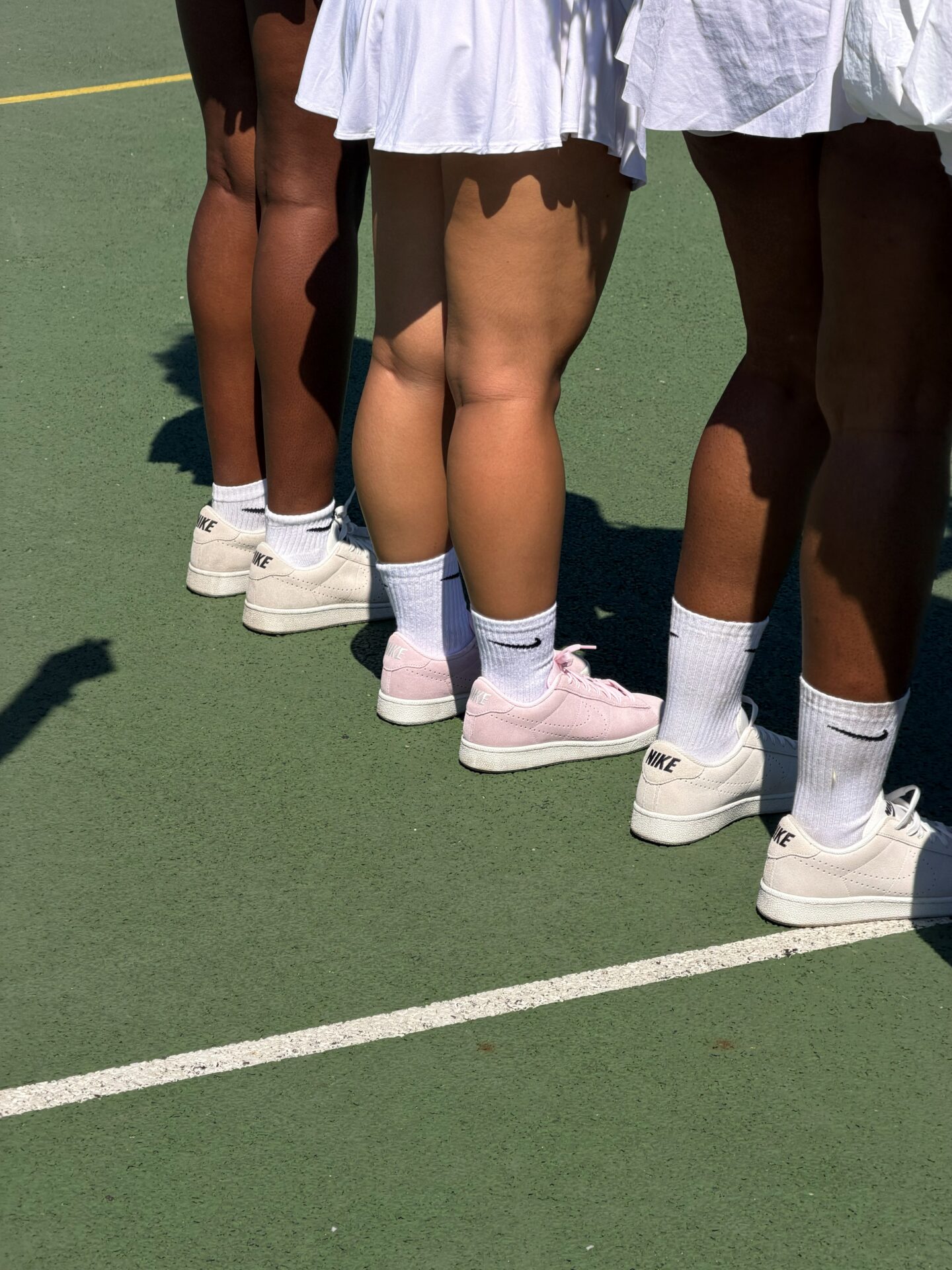 SheCanServe community wearing Nike Tennis Classic trainers, two in white and one in the pink colourway, with white Nike socks.
