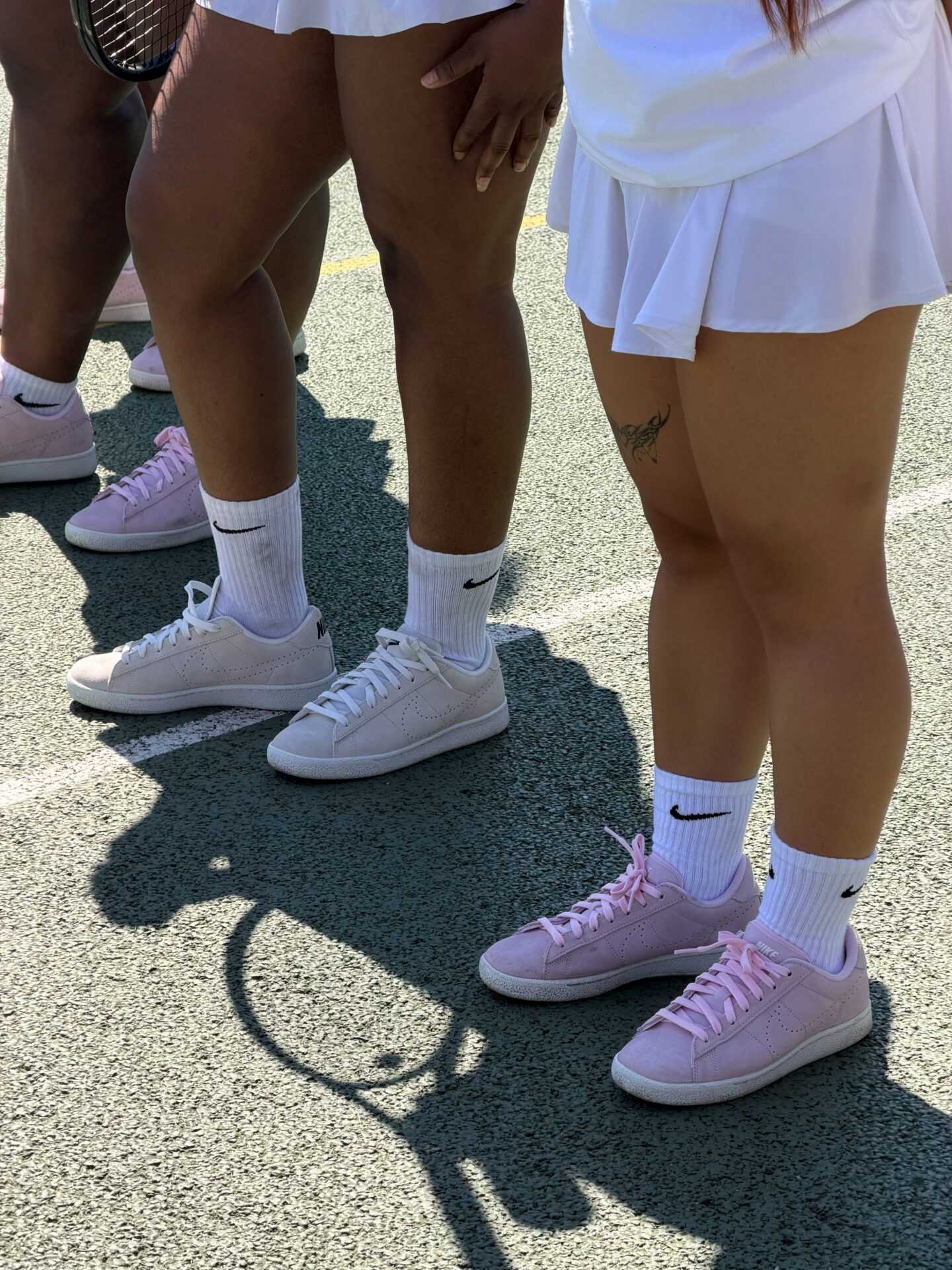 SheCanServe community wearing Nike Tennis Classic trainers, one in white and three in the pink colourway, with white Nike socks.