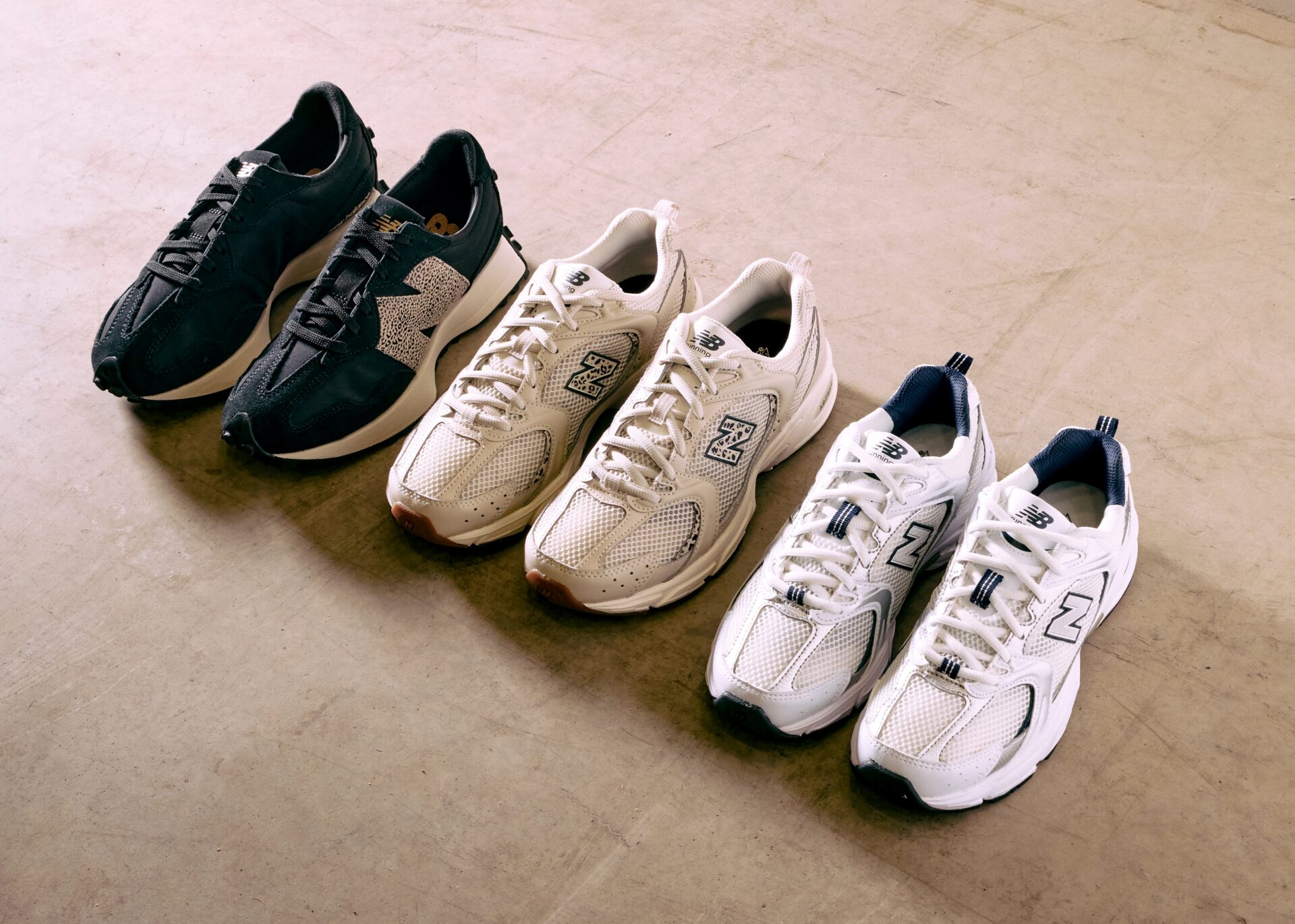 Three pairs of New Balance trainers sitting next to each other: one black pair of 327s, beige 740s, and white 530s.